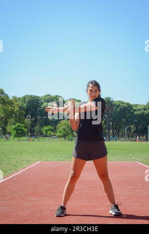 young woman on the track standing looking at the camera, she is stretching warming up before training, vertical image with copy space. Stock Photo