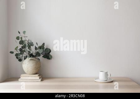 Minimal breakfast still life. Cup of coffee, tea. Empty white wall in sunlight table. Textured vase with silver eucalyptus leaves, branches on old Stock Photo