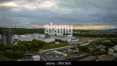 Sunset color in stormy sky over industrial manufacturing plant at edge of town Stock Photo
