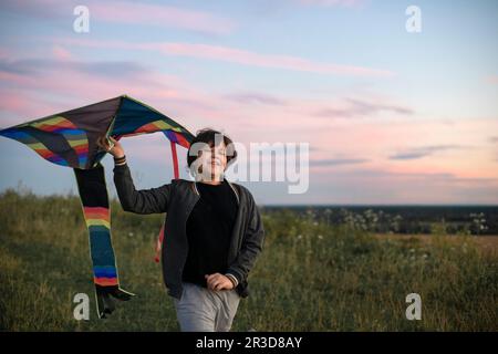 A teenager launches a kite at sunset in the summer in a field. The concept of hobbies, recreation and entertainment.  Stock Photo