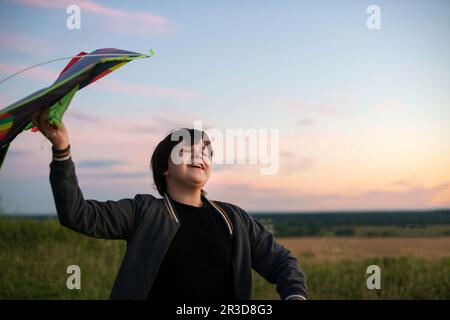 A teenager launches a kite at sunset in the summer in a field. The concept of hobbies, recreation and entertainment.  Stock Photo