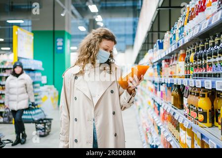 Young woman customer carefully reads the composition on the label of pumpkin carrot juice in a supermarket. The concept of proper nutrition and the choice of quality products without additives and dyes Stock Photo