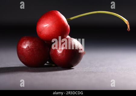 four ripe red cherries in an unusual pose on a dark background with oblique light represent freshness summer sweetness taste Stock Photo