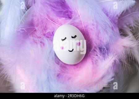 Funny smiley painted egg face in bird feather. Easter decorations. Copy space for text. Pastel colors. Easter greeting card. Stock Photo