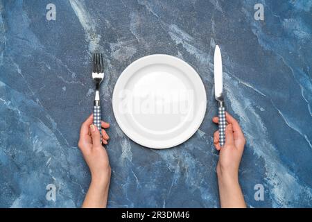 Female hands with empty plate and cutlery on blue marble background Stock Photo