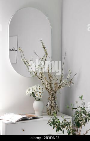 Vases with chrysanthemum flowers and blooming tree branches on chest of drawers in bedroom Stock Photo