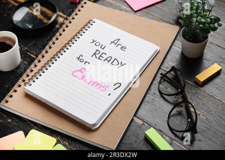 Notebooks with question ARE YOU READY FOR EXAM?, cup of coffee and magnifier on black wooden background Stock Photo