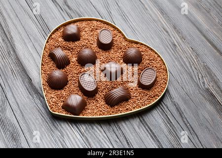 Chocolate candies in chocolate chips in a heart-shaped box on a dark wooden background top view, Valentine's Day. Stock Photo
