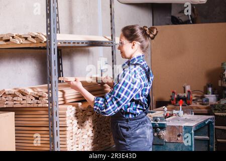 Female apprentice checking wooden plank at carpentry workshop Stock Photo