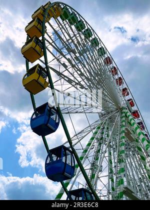 A jumbo sized Ferris Wheel ride looms high above against the backdrop of a blue sky with clouds on a bright summer day. Stock Photo