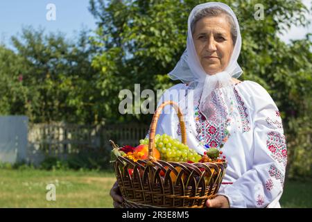 grandmother holds a full basket of fruits in her hands in the summer yard Stock Photo