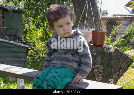 Curly little boy resting on a bench in the village Stock Photo