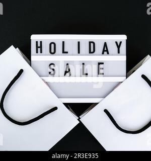 Light board with text HOLIDAY SALE with paper shopping bags. Big Sale online shopping concept. Promotion advertising. Holiday Stock Photo