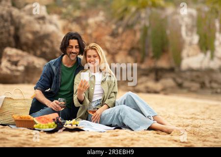 Romantic young couple taking selfie while having picnic at the beach Stock Photo