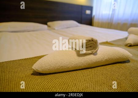 Hotel room with freshly made bed, perfectly clean and ironed sheets, stack of new folded towels in natural sun light. Stock Photo
