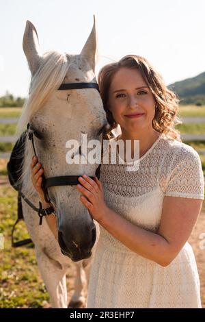 Portrait of a young woman in a white dress hugging horse Stock Photo