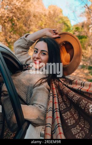 Brunette European looking cute girl sitting in a car enjoying sunny autumn weekend. Travel and road trip. Woman looking at the v Stock Photo