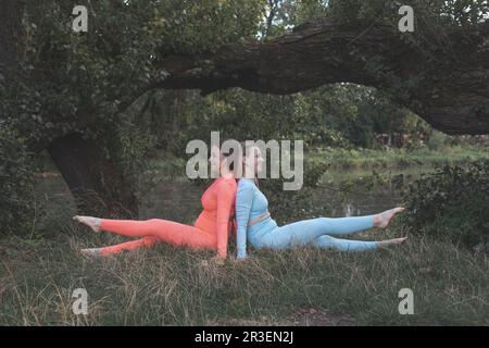 Two happy young girlfriends practice yoga outdoors Stock Photo