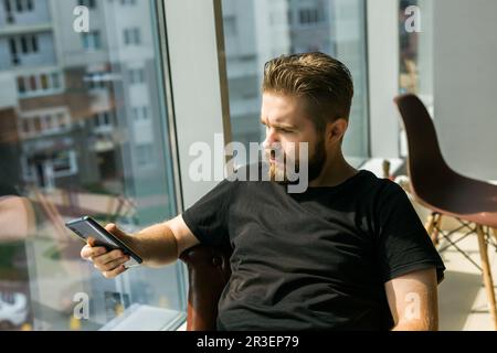 Fashionable young bearded guy wears stylish clothes and trendy hairstyle and happy to exchange messages with friends and uses free internet connection Stock Photo
