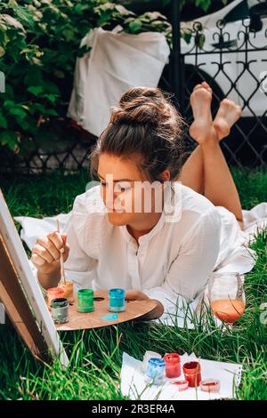 Artist painting on the easel outdoors in the garden. Open air outdoor art workshop. Draw on the canvas with brush and palette si Stock Photo