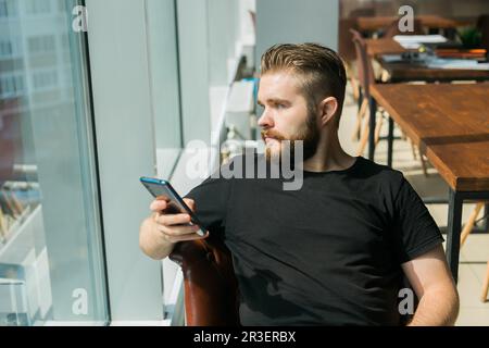 Fashionable young bearded guy wears stylish clothes and trendy hairstyle and happy to exchange messages with friends and uses free internet connection Stock Photo