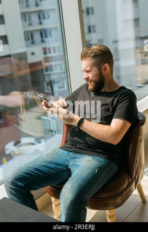 Fashionable young bearded guy wears stylish clothes and trendy hairstyle and happy to exchange messages with friends and uses free internet connection Stock Photo