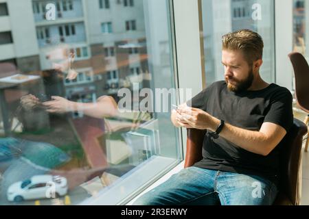 Fashionable young bearded guy wears stylish clothes and trendy hairstyle and happy to exchange messages with friends and uses free internet connection Stock Photo