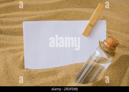 Sheet of white paper with copy space clothespin Paper Message in a glass bottle with a cork on the sand. Summer vacation holiday Stock Photo