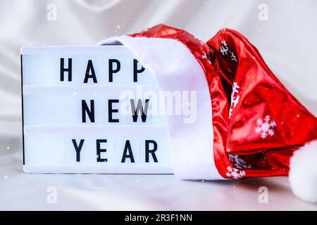 Lightbox with text HAPPY NEW YEAR with santa hat on silk fabric background. Winter holiday concept. Stock Photo