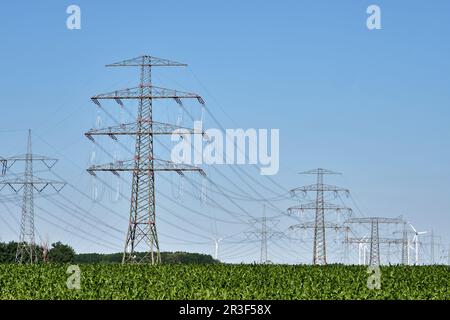 Electricity pylons and power lines with wind turbines in the back seen in Germany Stock Photo