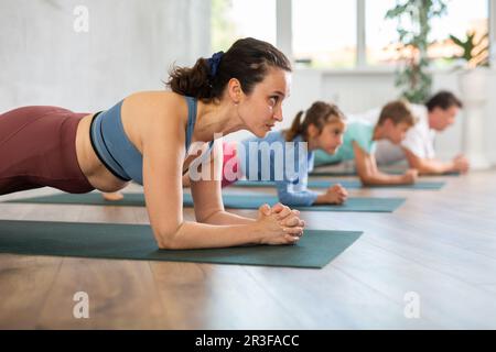 Willing middle-aged woman practicing table pose of yoga with her family ...