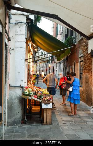 Two ladies chatting with a greengrocer outside his fruit and vegetable shop in a narrow alley in the sestiere of Cannaregio, Venice, Veneto, Italy Stock Photo
