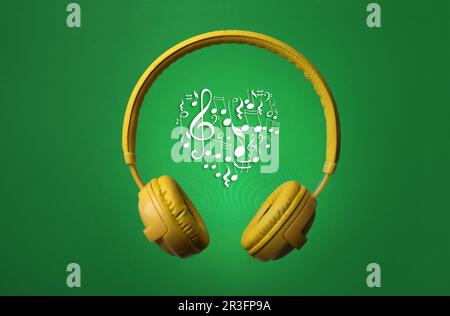 Yellow headphones and heart shape made of music notes with treble clef on green background Stock Photo