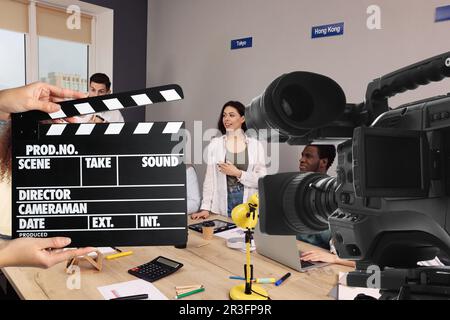 Shooting movie. Second assistant camera holding clapperboard near video camera in front of coworkers (actors) at office (film set) Stock Photo