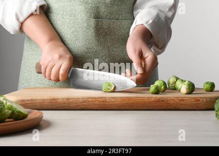 Woman cutting fresh brussel sprouts on board at wooden table, closeup Stock Photo