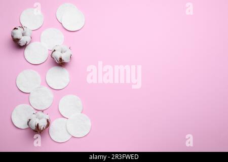 Soft clean cotton pads and flowers on pink background, flat lay. Space for text Stock Photo