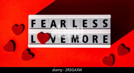 Lightbox with text FEAR LESS LOVE MORE. Motivational Words Quotes Concept with red hearts. Colorful red background. Minimalistic Stock Photo