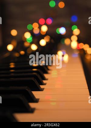 Piano keyboard with fairy lights and colorful blurred Christmas lights, seasonal background Stock Photo