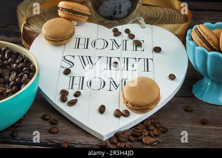 Coffee flavored macarons with coffee beans and cups of coffee. Lettering home sweet home on the heart. Stock Photo