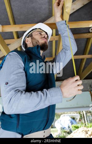 man measuring metal bar in roof space Stock Photo