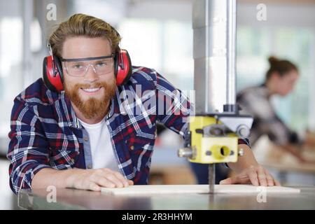 smiling joiner using drilling machine to make drawer at workshop Stock Photo