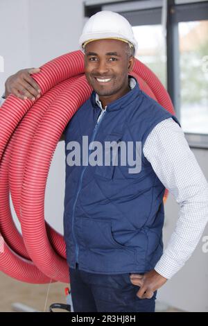 builder carrying reel of red pipe on his shoulder Stock Photo