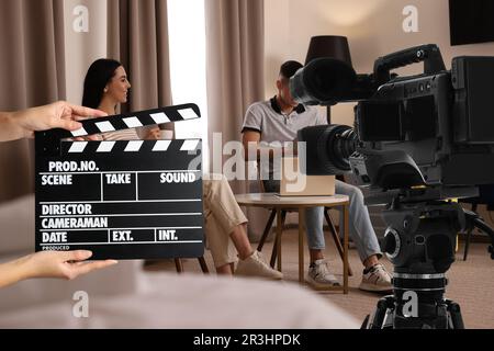 Shooting movie. Second assistant camera holding clapperboard near video camera in front of couple (actors) at hotel (film set) Stock Photo