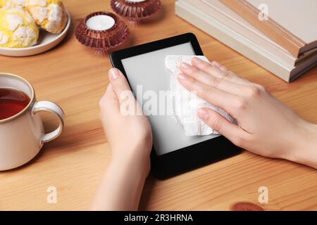 Woman wiping smartphone with paper at wooden table, closeup Stock Photo