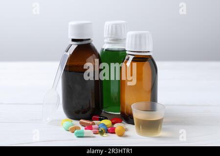 Bottles of syrup, measuring cup, dosing spoon and pills on white table. Cold medicine Stock Photo