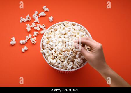 Woman taking fresh popcorn from bucket on orange background, above view Stock Photo