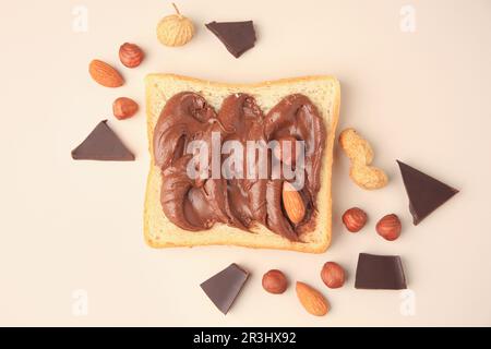 Tasty toast with chocolate paste and nuts on beige background, flat lay Stock Photo