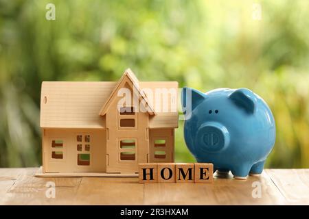 Piggy bank, house model and word Home made of cubes on wooden table outdoors Stock Photo