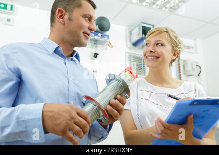 man showing metal part to smiling woman with clipboard Stock Photo