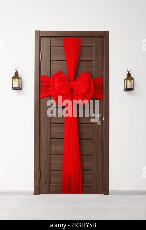 Wooden door with beautiful red bow and lanterns hanging on wall. Christmas decoration Stock Photo
